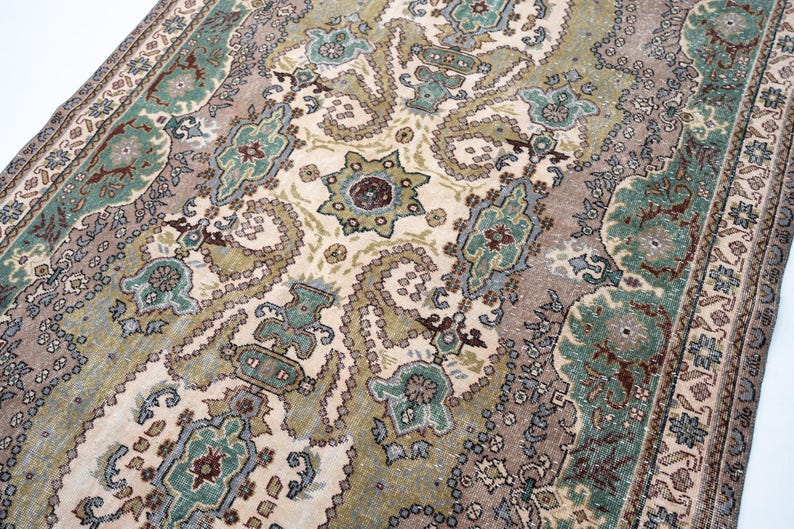May include: A rectangular area rug featuring an intricate pattern of paisley and floral motifs in shades of sage green, muted brown, cream, and dark red. The design includes a central medallion and a detailed border with repeating geometric shapes.