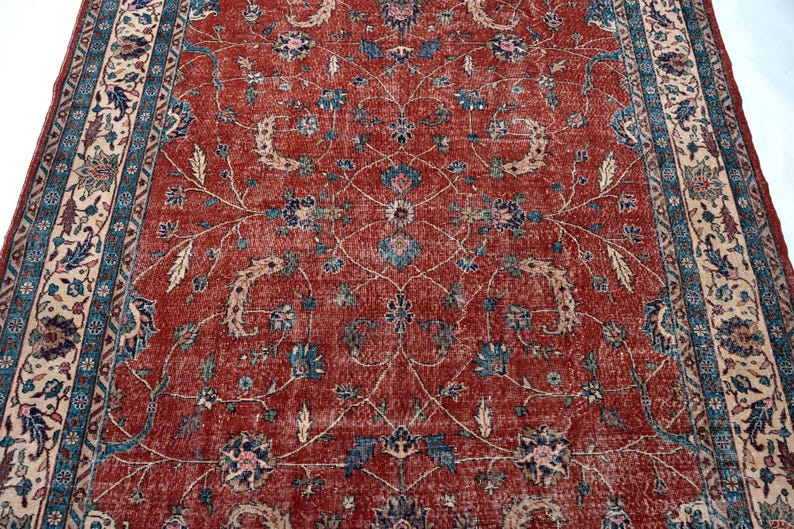 May include: A distressed, rectangular rug with a rich red background and intricate floral patterns in blue, beige, and cream. The rug features a detailed border with similar floral motifs, creating a classic, vintage aesthetic.