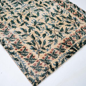 May include: Beige rug with a floral pattern. The rug features a repeating design of green leaves and red flowers on a beige background. The border has a similar floral pattern. The rug is rectangular.