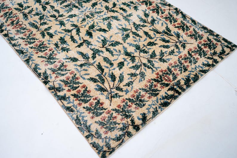 May include: Beige rug with a floral pattern. The rug features a repeating design of green leaves and red flowers on a beige background. The border has a similar floral pattern. The rug is rectangular.
