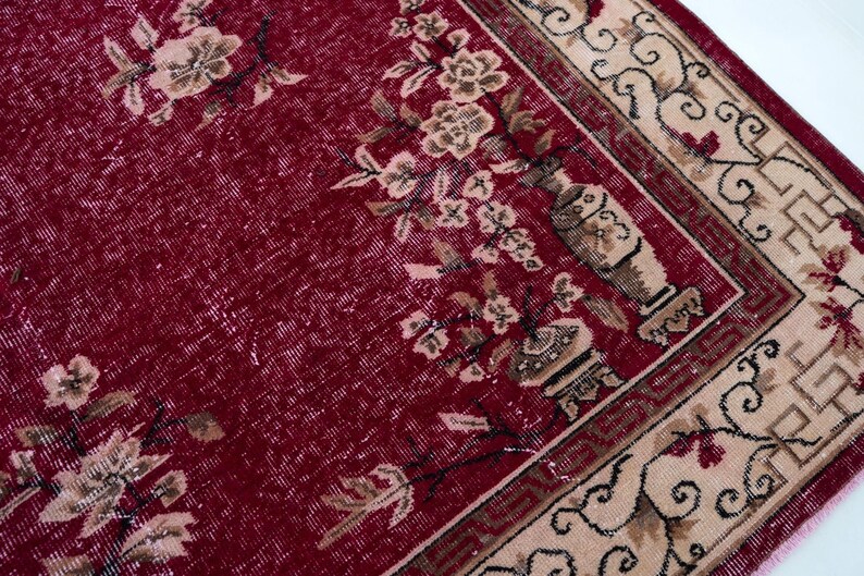 May include: A vintage red rug with a floral pattern and a beige border. The rug features a central field of deep red with faded floral motifs in beige and brown. The border has an intricate design with floral and geometric elements.
