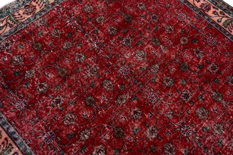 K&ouml;nnte beinhalten: Nahaufnahme eines roten Vintage-Teppichs mit einem komplizierten Blumenmuster. Der Teppich hat einen Used-Look mit verblassten Farben und einem detaillierten Rand. Das Design umfasst verschiedene florale und geometrische Elemente.