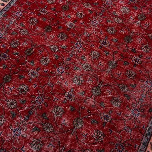 K&ouml;nnte beinhalten: Ein roter, abgenutzter Teppich mit einem komplizierten Blumenmuster. Der Teppich hat ein rotes Mittelfeld mit verblassten Blumenmotiven in Braun-, Blau- und Cremet&ouml;nen. Ein Rand mit einem Blumendesign in Rosa und Blau umrahmt den Teppich.
