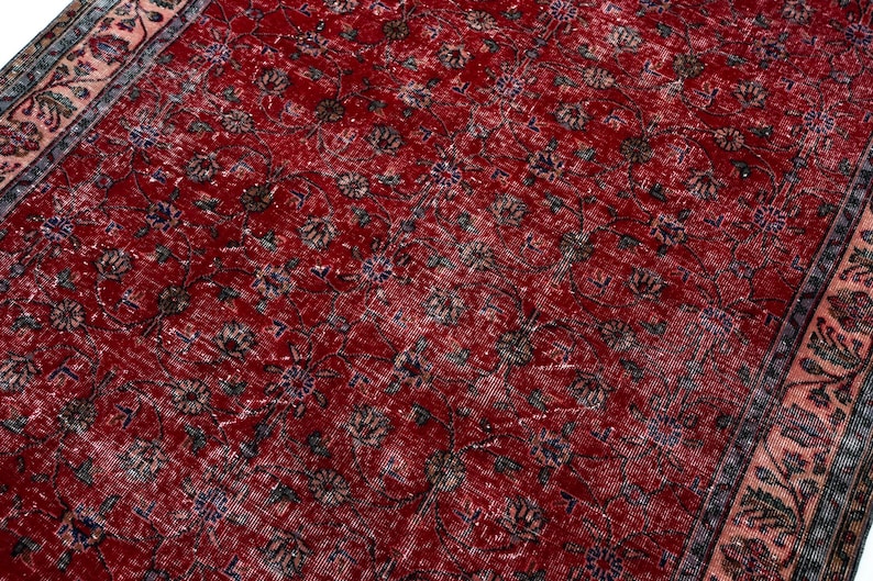 K&ouml;nnte beinhalten: Ein roter, abgenutzter Teppich mit einem komplizierten Blumenmuster. Der Teppich hat ein rotes Mittelfeld mit verblassten Blumenmotiven in Braun-, Blau- und Cremet&ouml;nen. Ein Rand mit einem Blumendesign in Rosa und Blau umrahmt den Teppich.