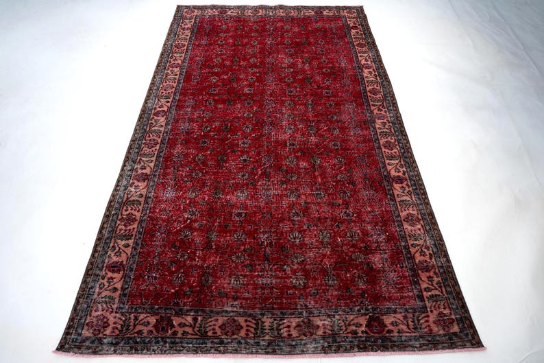 K&ouml;nnte beinhalten: Ein rechteckiger, verwaschen roter Teppich mit detailliertem Blumenmuster. Der Teppich hat einen dunklen Rand mit einem helleren rosa Innenrand. Das Mittelfeld ist tiefrot mit einem sich wiederholenden Blumendesign. Geeignet f&uuml;r Wohn- und Schlafzimmer.