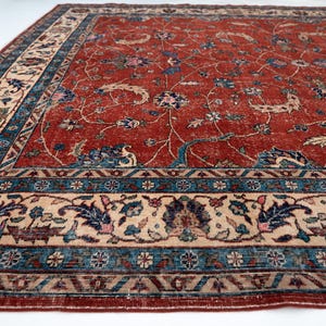 May include: A large, rectangular rug with a distressed, vintage appearance. The rug features a deep red central field with a floral pattern in blue, beige, and green. A detailed border in similar colors frames the design.