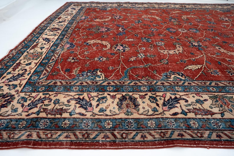 May include: A large, rectangular rug with a distressed, vintage appearance. The rug features a deep red central field with a floral pattern in blue, beige, and green. A detailed border in similar colors frames the design.