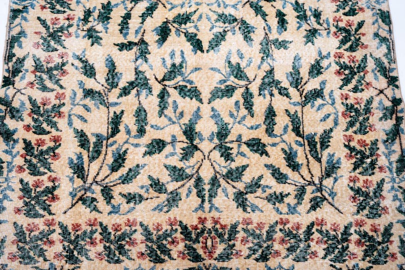 May include: Beige rug with a repeating pattern of teal and blue leaves and red flowers. The floral design is symmetrical, with a border of red flowers. The rug has a vintage, distressed look.