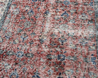 May include: Close-up of a distressed, vintage rug with a detailed floral pattern. The rug features a red and cream central field with blue and cream floral accents. The border is cream with a blue and cream floral design.