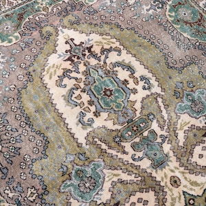 May include: A rectangular area rug featuring a central cream-colored medallion surrounded by intricate floral and geometric patterns in shades of sage green, dusty rose, slate blue, and dark brown, with a detailed border framing the entire design.
