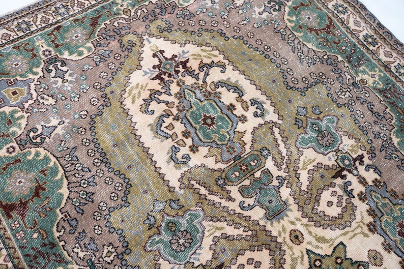 May include: A rectangular area rug featuring a central cream-colored medallion surrounded by intricate floral and geometric patterns in shades of sage green, dusty rose, slate blue, and dark brown, with a detailed border framing the entire design.
