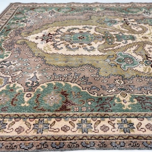 May include: A rectangular area rug featuring a complex pattern with shades of sage green, dusty rose, cream, and dark brown. The design includes a central medallion surrounded by intricate floral and geometric motifs, finished with a detailed border.