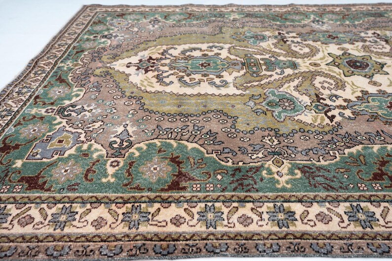May include: A rectangular area rug featuring a complex pattern with shades of sage green, dusty rose, cream, and dark brown. The design includes a central medallion surrounded by intricate floral and geometric motifs, finished with a detailed border.