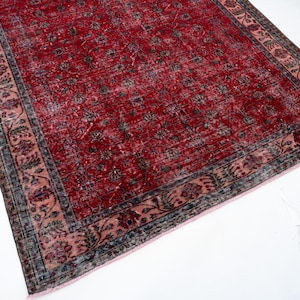 K&ouml;nnte beinhalten: Ein rechteckiger Teppich im Vintage-Stil mit einem tiefroten Feld und einem floralen Muster. Der Rand weist ein erg&auml;nzendes Design in Rosa-, Blau- und Gr&uuml;nt&ouml;nen auf. Der Teppich liegt auf einer wei&szlig;en Oberfl&auml;che.