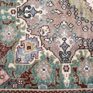May include: A woven rug featuring a complex geometric and floral pattern in shades of teal, taupe, cream, and dark brown. The design includes intricate borders and central motifs with repeating symmetrical shapes and detailed botanical elements.
