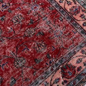 K&ouml;nnte beinhalten: Nahaufnahme eines abgenutzten roten Teppichs mit floralen Mustern. Der Teppich hat ein rotes Mittelfeld mit verblassten Blumenmotiven in Blau, Grau und Creme. Ein Rand in Rosa- und Graut&ouml;nen umrahmt das Design und erzeugt eine Vintage-&Auml;sthetik.