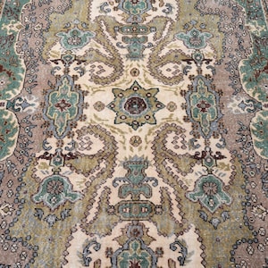 May include: A rectangular area rug featuring a complex central medallion and intricate floral motifs in shades of sage green, dusty rose, cream, and deep maroon. The border displays a repeating geometric pattern with stylized botanical elements.