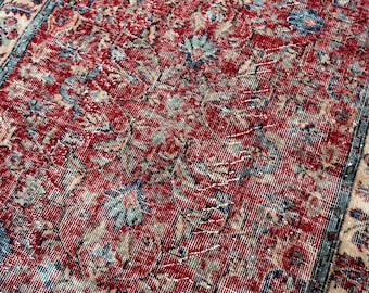 May include: A rectangular area rug featuring a deep red field with intricate floral and vine patterns in shades of blue, beige, and cream. The rug has a wide border with repeating botanical motifs in matching colors and a distressed texture.