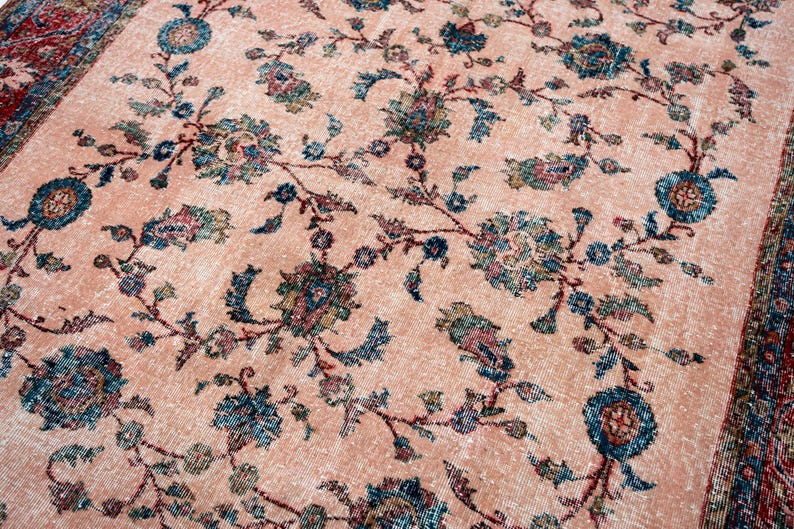 Pu&ograve; includere: Un tappeto vintage dall'aspetto sbiadito e usurato. Il tappeto presenta un campo centrale color pesca adornato da un motivo floreale in verde acqua, blu e rosso tenue. Il bordo &egrave; rosso scuro con disegni intricati.