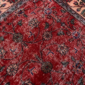 K&ouml;nnte beinhalten: Nahaufnahme eines roten Vintage-Teppichs mit einem komplizierten Blumenmuster. Der Teppich hat einen Used-Look mit verblassten Farben, darunter Rot, Blau und Beige. Das Design umfasst Blumen- und Rankenmotive.