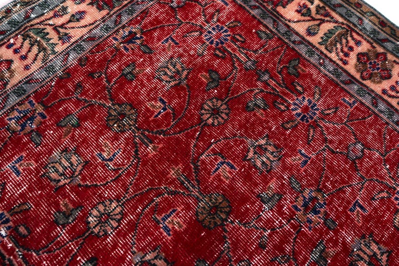 K&ouml;nnte beinhalten: Nahaufnahme eines roten Vintage-Teppichs mit einem komplizierten Blumenmuster. Der Teppich hat einen Used-Look mit verblassten Farben, darunter Rot, Blau und Beige. Das Design umfasst Blumen- und Rankenmotive.