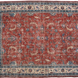 May include: Rectangular red rug with an intricate floral pattern. The rug features a central field of red with a detailed design of blue and beige floral motifs. A border of blue and beige floral patterns frames the rug.