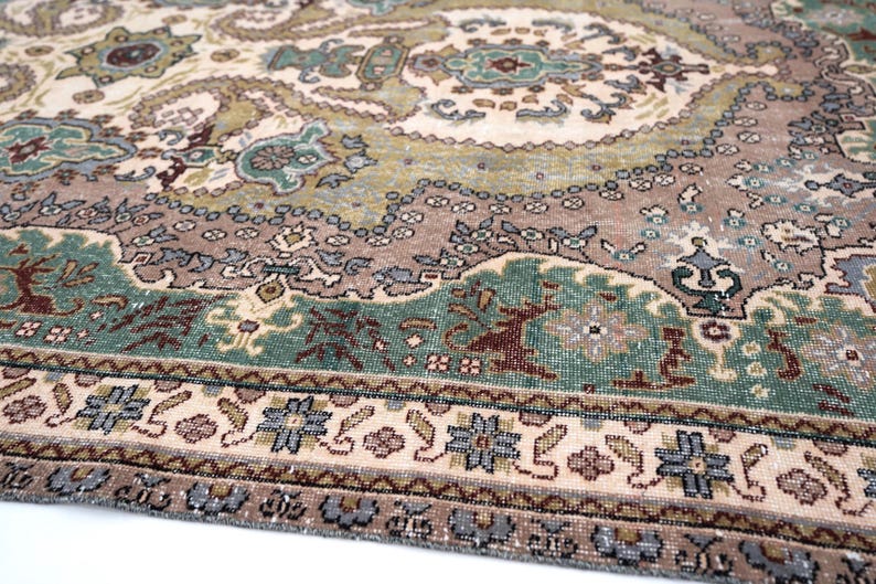 May include: A woven area rug featuring a complex pattern of paisley and floral motifs in shades of sage green, dusty rose, cream, and slate blue. The design includes a central medallion and a detailed border with repeating geometric flower shapes.
