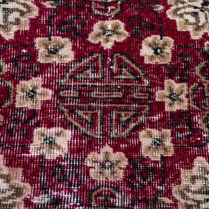 May include: Close-up of a red and beige oriental rug with a floral pattern. The rug features a central medallion and repeating floral motifs in beige and brown against a red background. The rug has a distressed, vintage appearance.