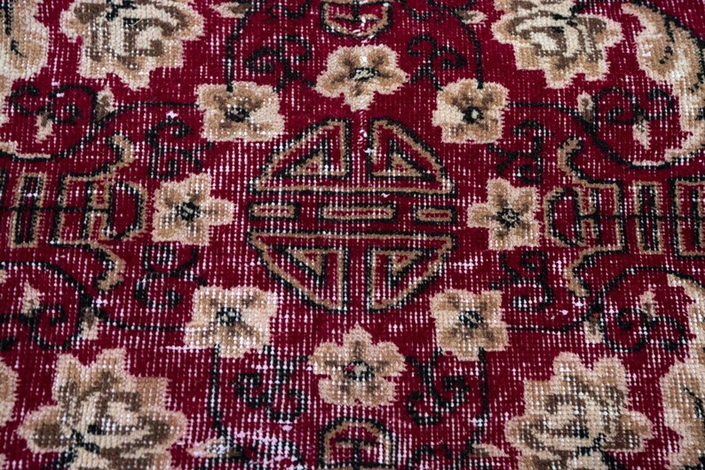May include: Close-up of a red and beige oriental rug with a floral pattern. The rug features a central medallion and repeating floral motifs in beige and brown against a red background. The rug has a distressed, vintage appearance.