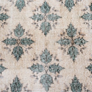 May include: A woven textile featuring a repeating diamond-shaped floral pattern in dark teal against a light beige background. The fabric displays a visible grid-like weave structure with consistent spacing between each symmetrical botanical motif.