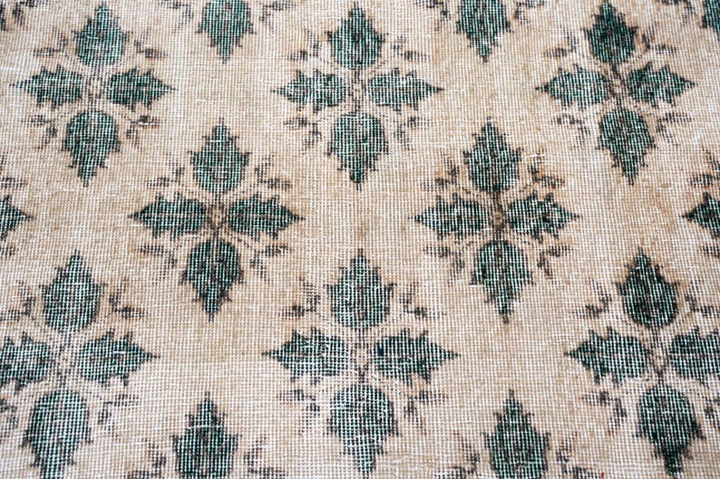 May include: A woven textile featuring a repeating diamond-shaped floral pattern in dark teal against a light beige background. The fabric displays a visible grid-like weave structure with consistent spacing between each symmetrical botanical motif.