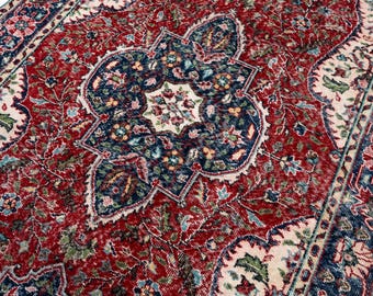 May include: A detailed close-up of a vintage rug with a central medallion design. The rug features a rich red background with intricate floral patterns in navy blue, cream, and green. The edges are bordered with a navy blue and cream design.