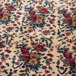 May include: Beige floral rug with a dark blue border. The rug features a repeating pattern of red, yellow, and purple flowers with green and blue leaves. The rug has a vintage, antique appearance.
