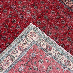 K&ouml;nnte beinhalten: Zwei antike rote Teppiche mit floralen Mustern. Ein Teppich ist vollst&auml;ndig sichtbar, w&auml;hrend der andere teilweise sichtbar ist, mit einer hochgeklappten Ecke, die einen detaillierten Rand mit cremefarbenen, blauen und rosa Akzenten zeigt. Die Teppiche haben einen Used-Look.