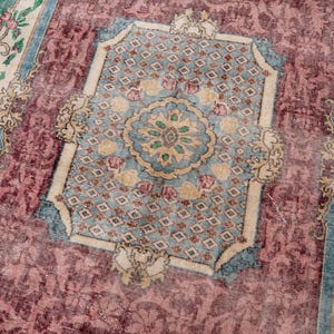 May include: A vintage rug with a central medallion design in shades of blue, beige, and green, set against a faded burgundy field. The rug features floral borders and intricate patterns, showcasing a distressed, antique aesthetic.