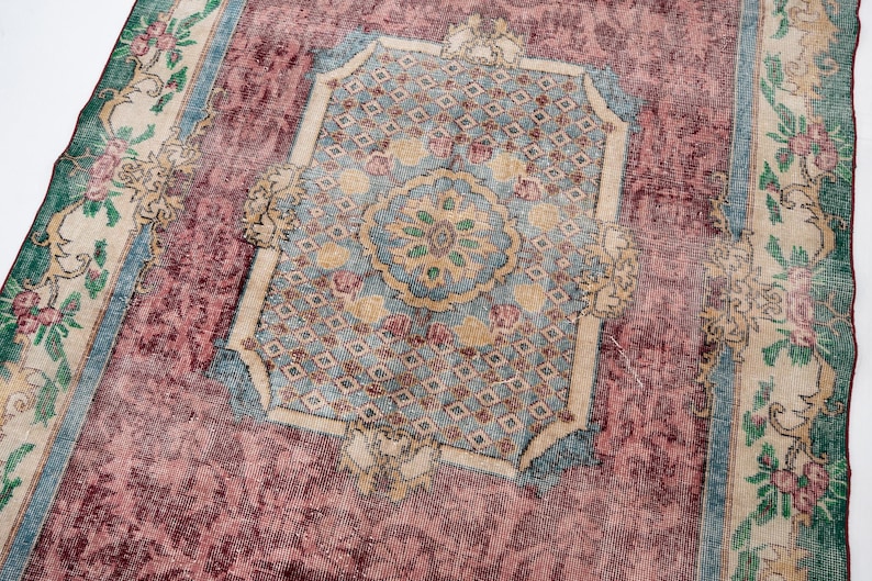 May include: A vintage rug with a central medallion design in shades of blue, beige, and green, set against a faded burgundy field. The rug features floral borders and intricate patterns, showcasing a distressed, antique aesthetic.