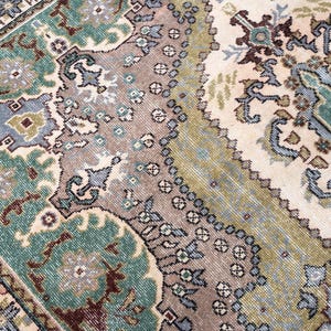 May include: A woven area rug featuring a complex pattern of floral and geometric motifs in shades of teal, sage green, cream, and muted brown. The design includes intricate borders and central medallions with symmetrical shapes and detailed linework.
