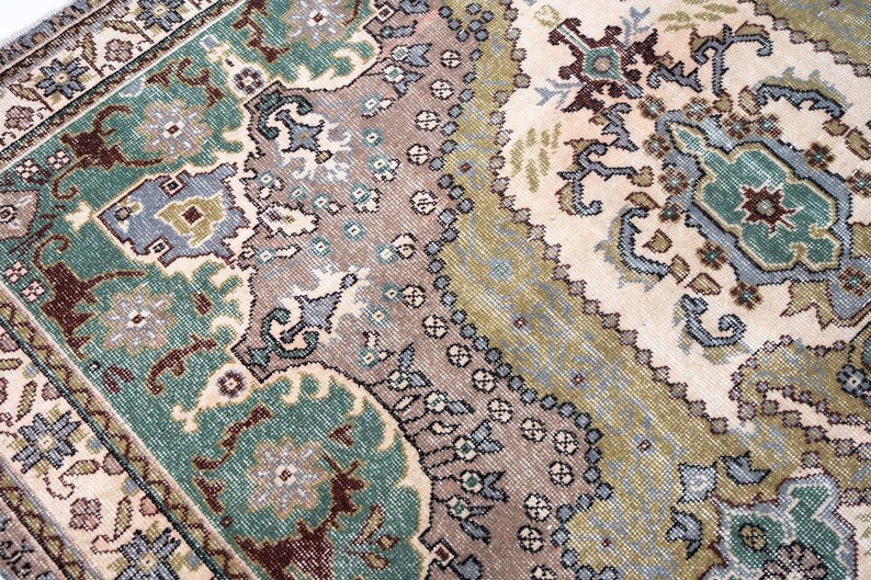 May include: A woven area rug featuring a complex pattern of floral and geometric motifs in shades of teal, sage green, cream, and muted brown. The design includes intricate borders and central medallions with symmetrical shapes and detailed linework.