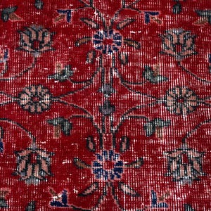 K&ouml;nnte beinhalten: Nahaufnahme eines roten Orientteppichs mit detailliertem Blumenmuster. Der Teppich hat einen Used-Look mit verblassten wei&szlig;en und blauen Akzenten, wodurch eine Vintage-&Auml;sthetik entsteht. Das Design umfasst stilisierte Blumen und Bl&auml;tter.