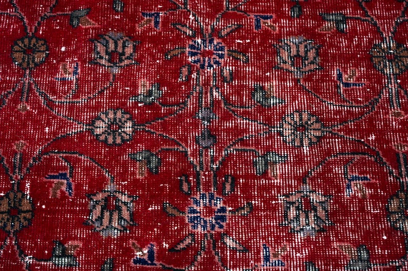 K&ouml;nnte beinhalten: Nahaufnahme eines roten Orientteppichs mit detailliertem Blumenmuster. Der Teppich hat einen Used-Look mit verblassten wei&szlig;en und blauen Akzenten, wodurch eine Vintage-&Auml;sthetik entsteht. Das Design umfasst stilisierte Blumen und Bl&auml;tter.
