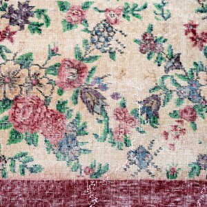 Pode incluir: Um tapete floral vintage com um centro creme e uma borda vermelha escura. O tapete apresenta um padr&atilde;o de flores e folhas rosa, roxas, azuis e verdes. O design do tapete &eacute; detalhado e intrincado, com uma apar&ecirc;ncia desbotada e antiga.