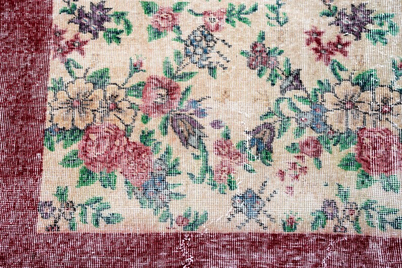 Pode incluir: Um tapete floral vintage com um centro creme e uma borda vermelha escura. O tapete apresenta um padr&atilde;o de flores e folhas rosa, roxas, azuis e verdes. O design do tapete &eacute; detalhado e intrincado, com uma apar&ecirc;ncia desbotada e antiga.