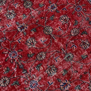 K&ouml;nnte beinhalten: Nahaufnahme eines abgenutzten roten Teppichs mit einem komplizierten Blumenmuster. Der Teppich hat ein rotes Mittelfeld mit verblassten wei&szlig;en, blauen und gr&uuml;nen Blumenmotiven. Das Design deutet auf einen Vintage- oder Antik-Stil hin.