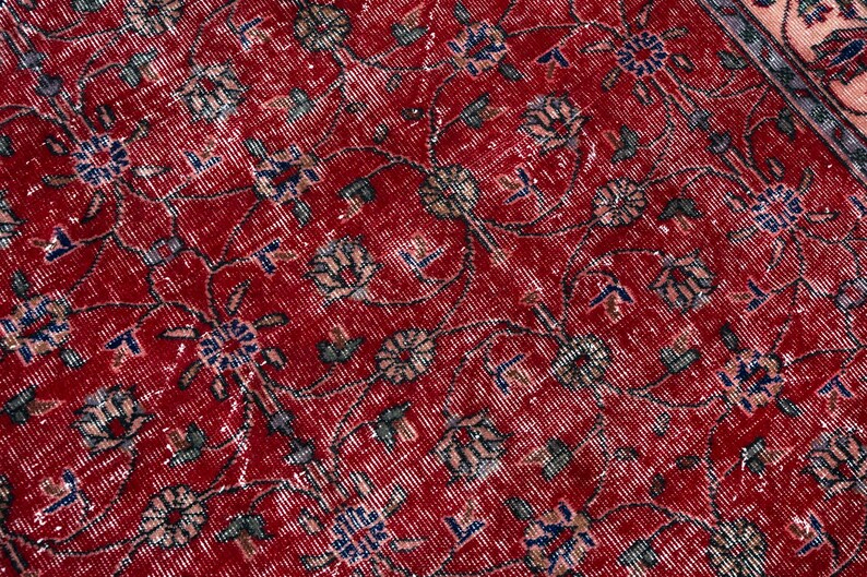 K&ouml;nnte beinhalten: Nahaufnahme eines abgenutzten roten Teppichs mit einem komplizierten Blumenmuster. Der Teppich hat ein rotes Mittelfeld mit verblassten wei&szlig;en, blauen und gr&uuml;nen Blumenmotiven. Das Design deutet auf einen Vintage- oder Antik-Stil hin.