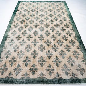 May include: A rectangular area rug featuring a repeating dark green floral pattern set against a light beige background. The rug is framed by a solid dark green border that runs along all four edges, creating a distinct contrast with the center.