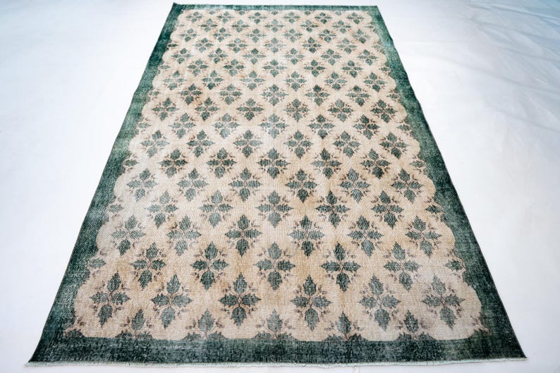 May include: A rectangular area rug featuring a repeating dark green floral pattern set against a light beige background. The rug is framed by a solid dark green border that runs along all four edges, creating a distinct contrast with the center.