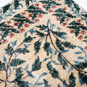 May include: Close-up of a beige rug with a floral pattern. The rug features green, blue, and red floral and leaf designs. The rug has a distressed, vintage look.