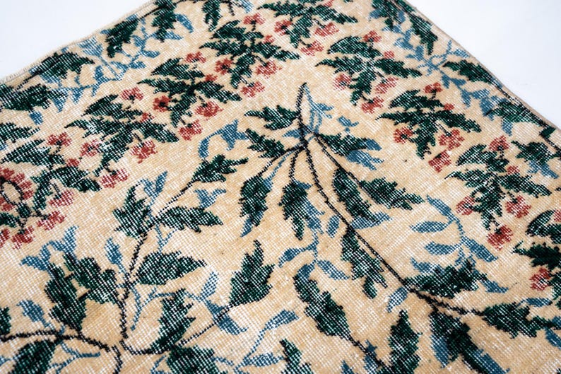 May include: Close-up of a beige rug with a floral pattern. The rug features green, blue, and red floral and leaf designs. The rug has a distressed, vintage look.