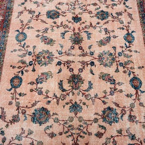 Pu&ograve; includere: Un tappeto rettangolare con un campo centrale color pesca e un motivo floreale dettagliato in verde acqua, blu e rosa tenue. Il bordo &egrave; rosso intenso con disegni intricati. Il design del tappeto &egrave; simmetrico e tradizionale.