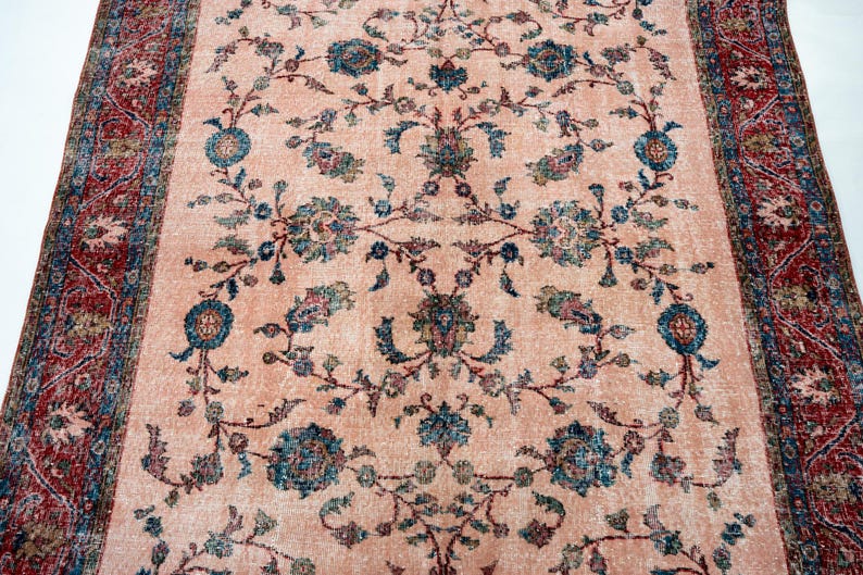 Pu&ograve; includere: Un tappeto rettangolare con un campo centrale color pesca e un motivo floreale dettagliato in verde acqua, blu e rosa tenue. Il bordo &egrave; rosso intenso con disegni intricati. Il design del tappeto &egrave; simmetrico e tradizionale.